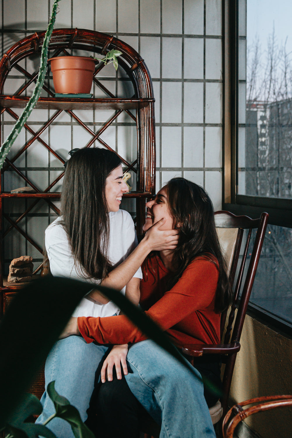 two woman smile as one sits on the other lap