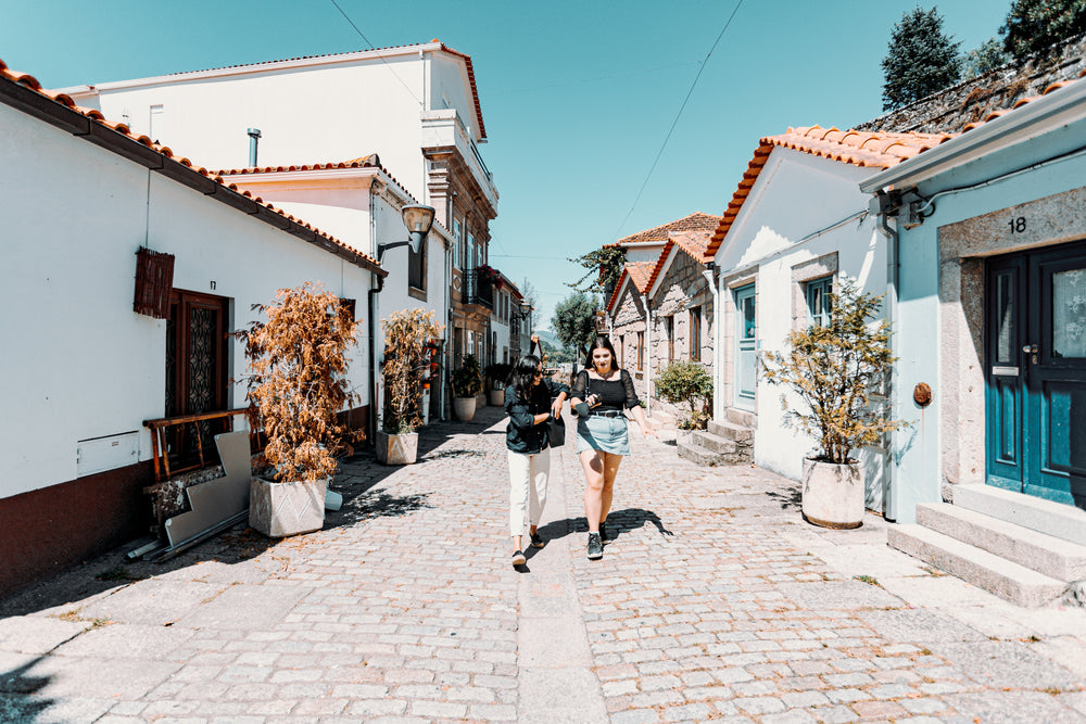 two woman walk down a pathway with buildings on each side