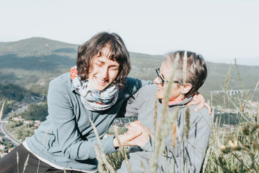 two women laugh together while sitting around tall grass