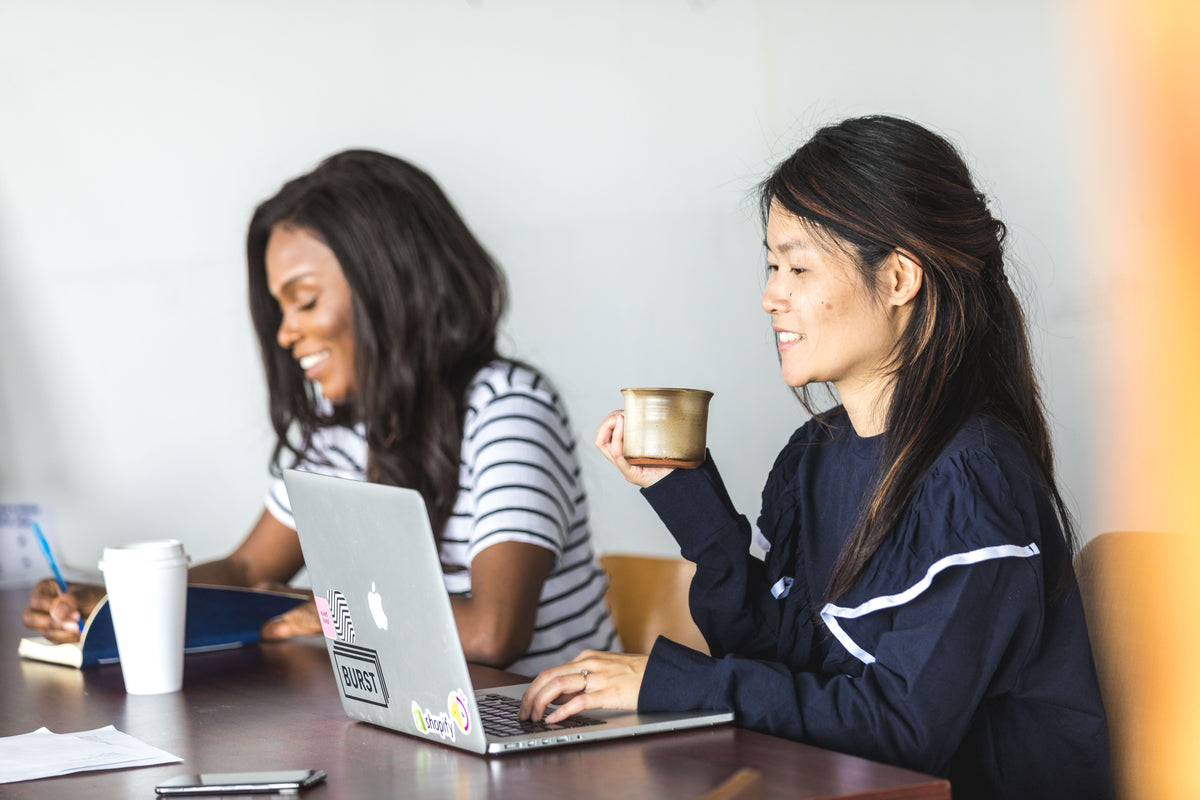 two women sit together getting work done
