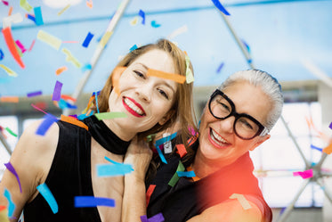 two women smiling in a blizzard of rainbow paper confetti