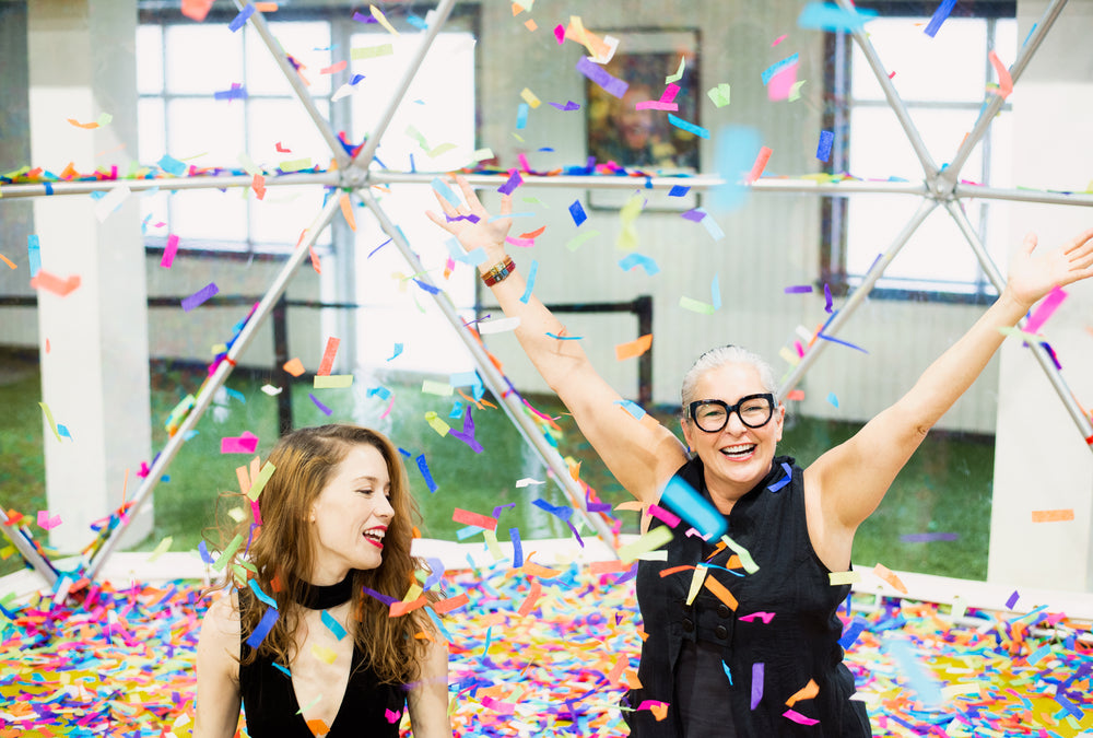 two women surrounded by rainbow confetti with arms raised