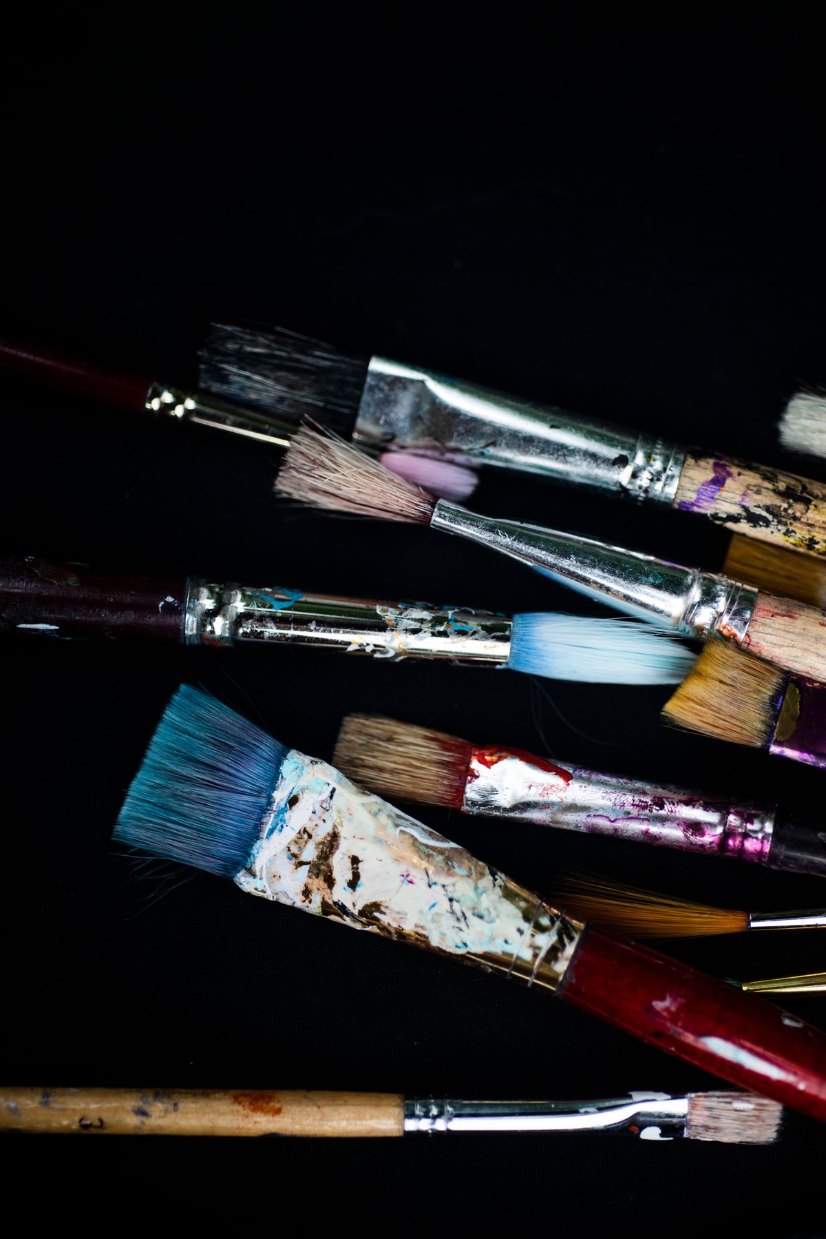 variety of colored paint brushes flatlay on black background