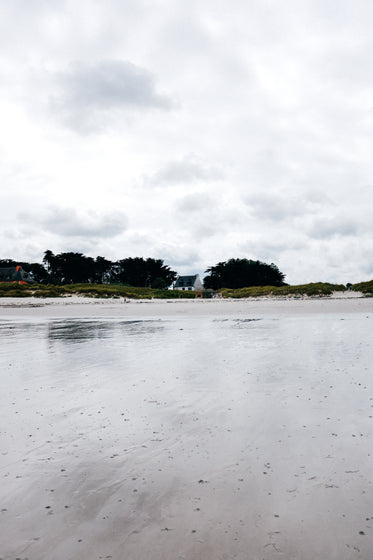 view of a distant house from a wet sandy beach