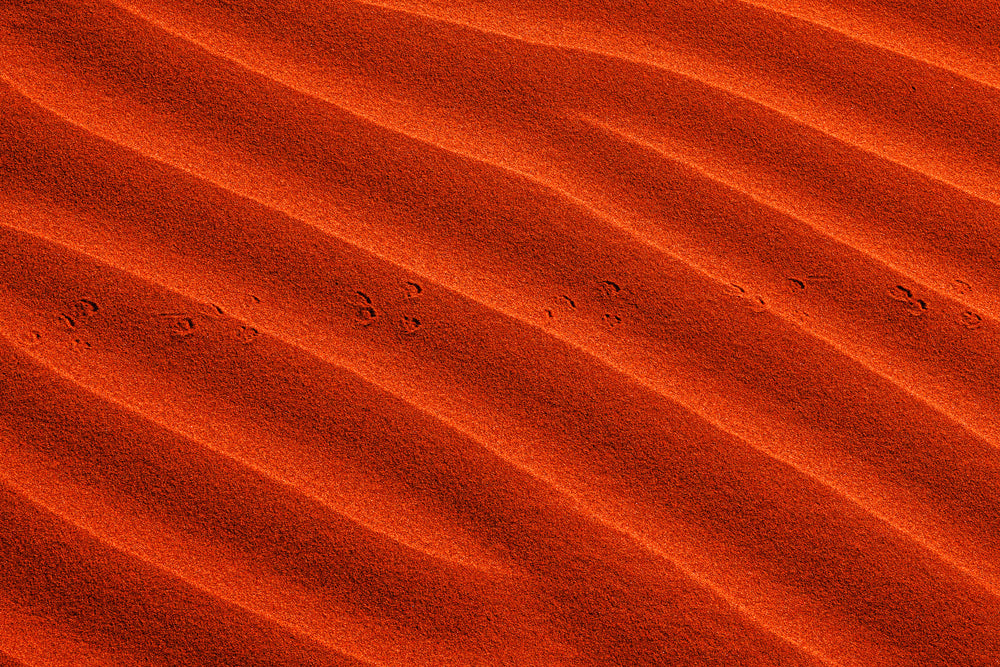 Waves In Vibrant Orange Sand With Small Footprints