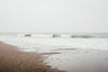 waves roll up to the sandy beach on a overcast day