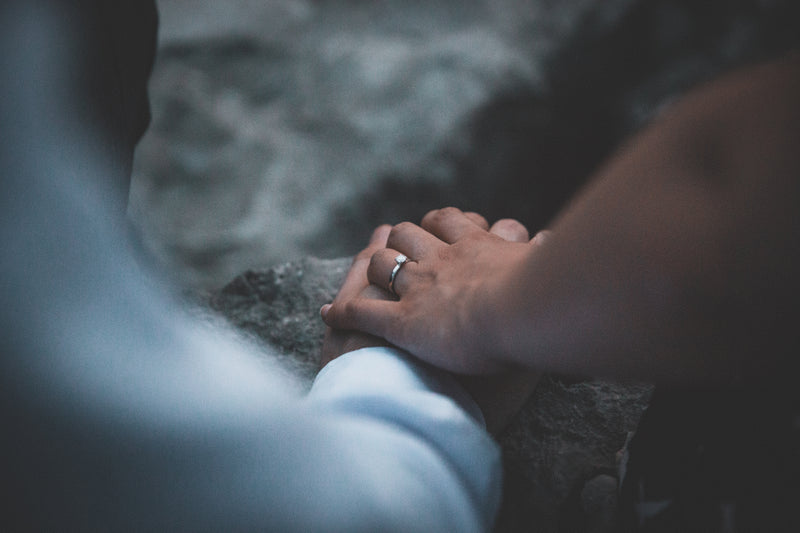 a person holding a ring on a rock - wedding rings couples hands