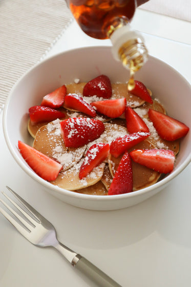 white bowl with mini pancakes with cut strawberries