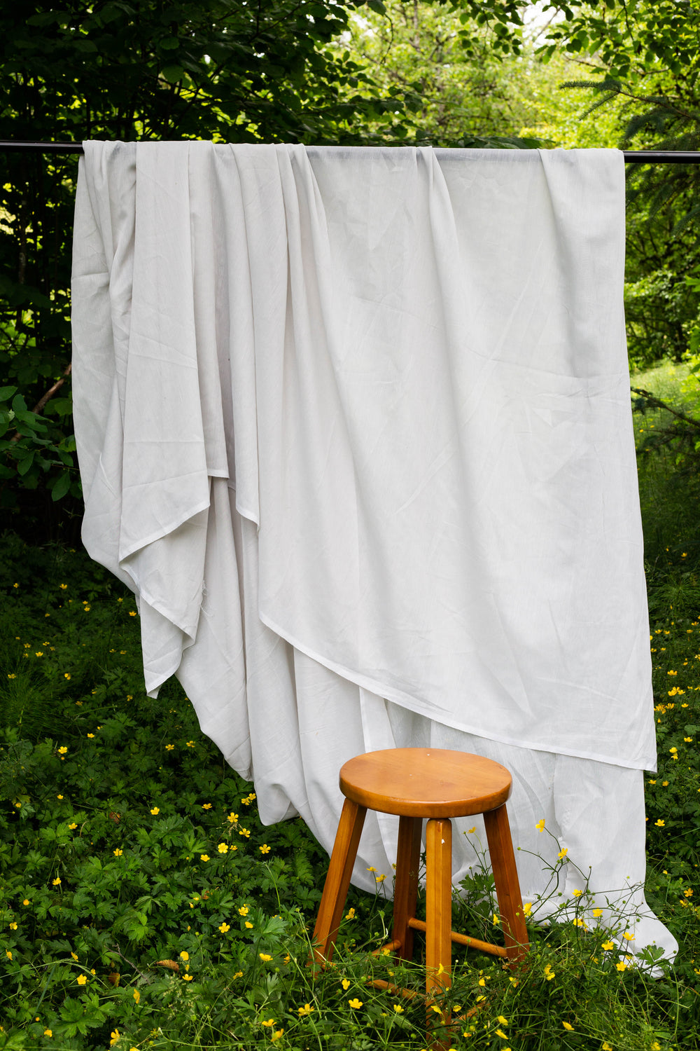 white flowing sheet outdoors with a wooden stool in front of it