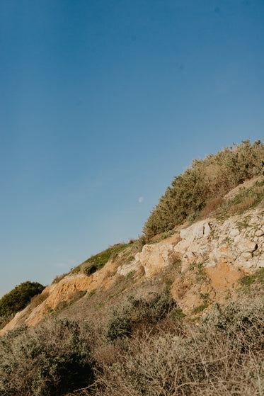 white moon on crisp blue daytime sky lined by rocky cliffs