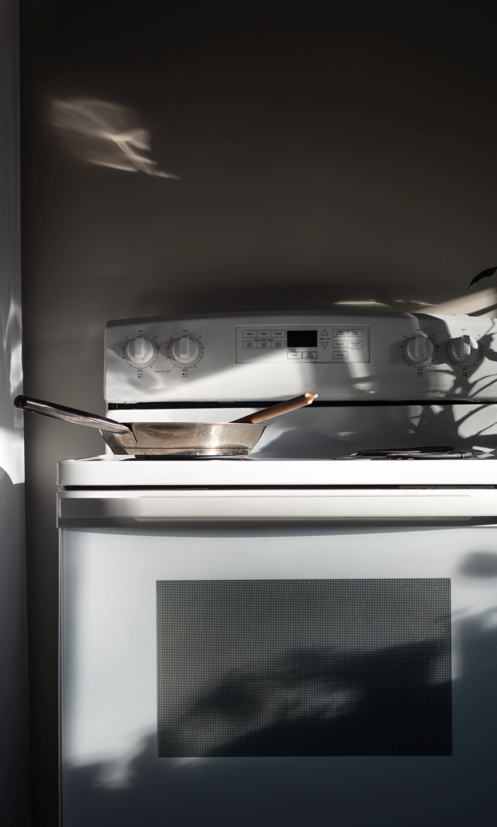 white stove with a silver pan is bathed in window light