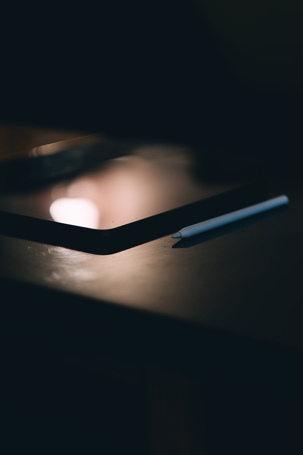 white stylus lays on a black tablet in dark room