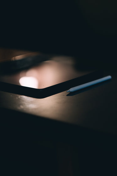 white stylus lays on a black tablet in dark room