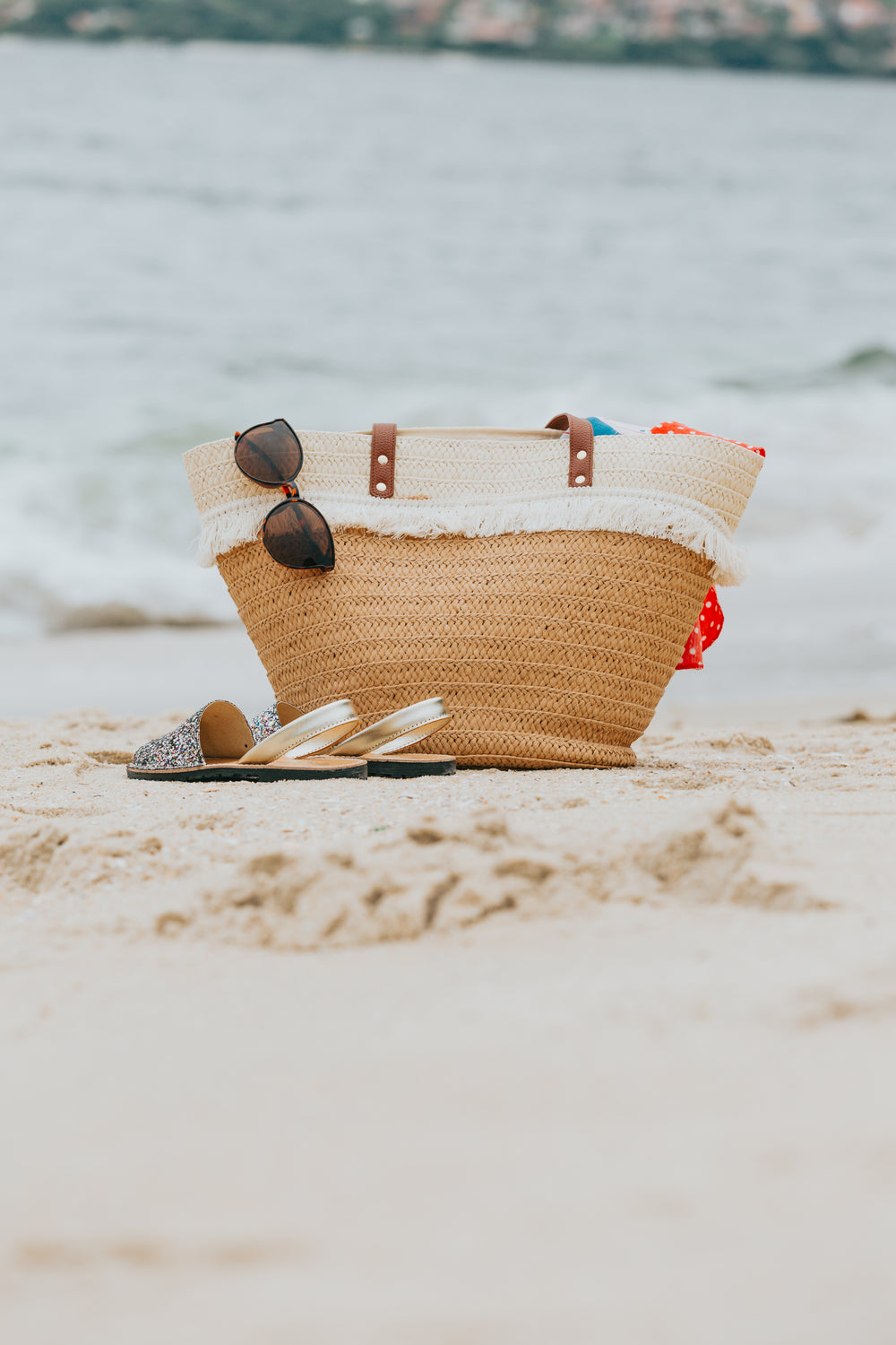 wicker beach bag and sandals on a white sandy beach