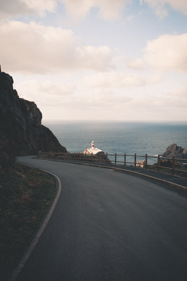 winding paved road with a lighthouse in the distance