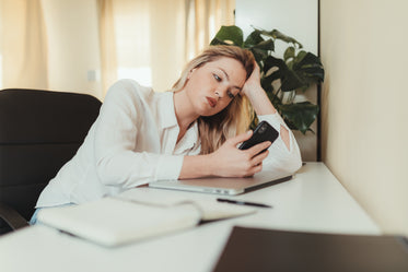 woman at a desk with laptop closed looking at her phone