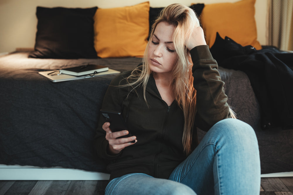 woman at the end of her bed looks at her phone