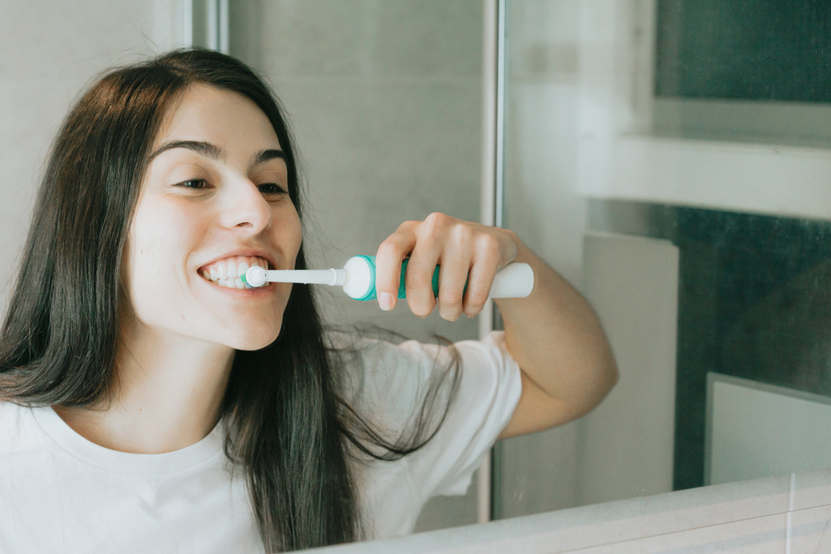 woman brushes with an electric toothbrush in a mirror