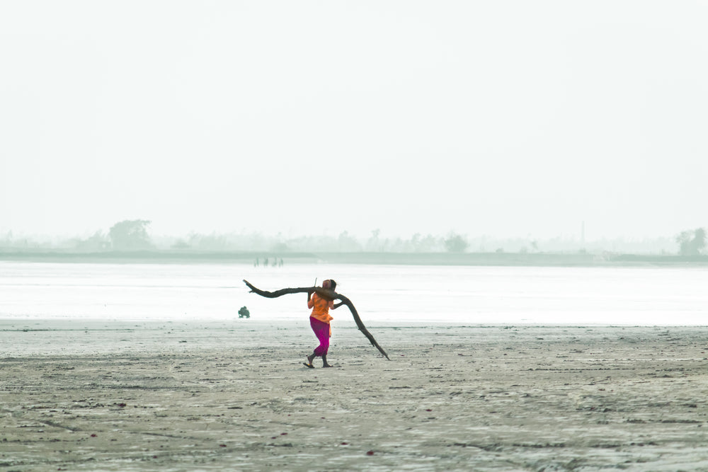 woman carries wood across beach in india