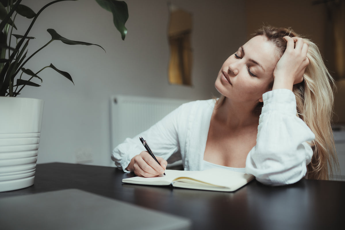 woman closes her eyes while journalling in a notebook
