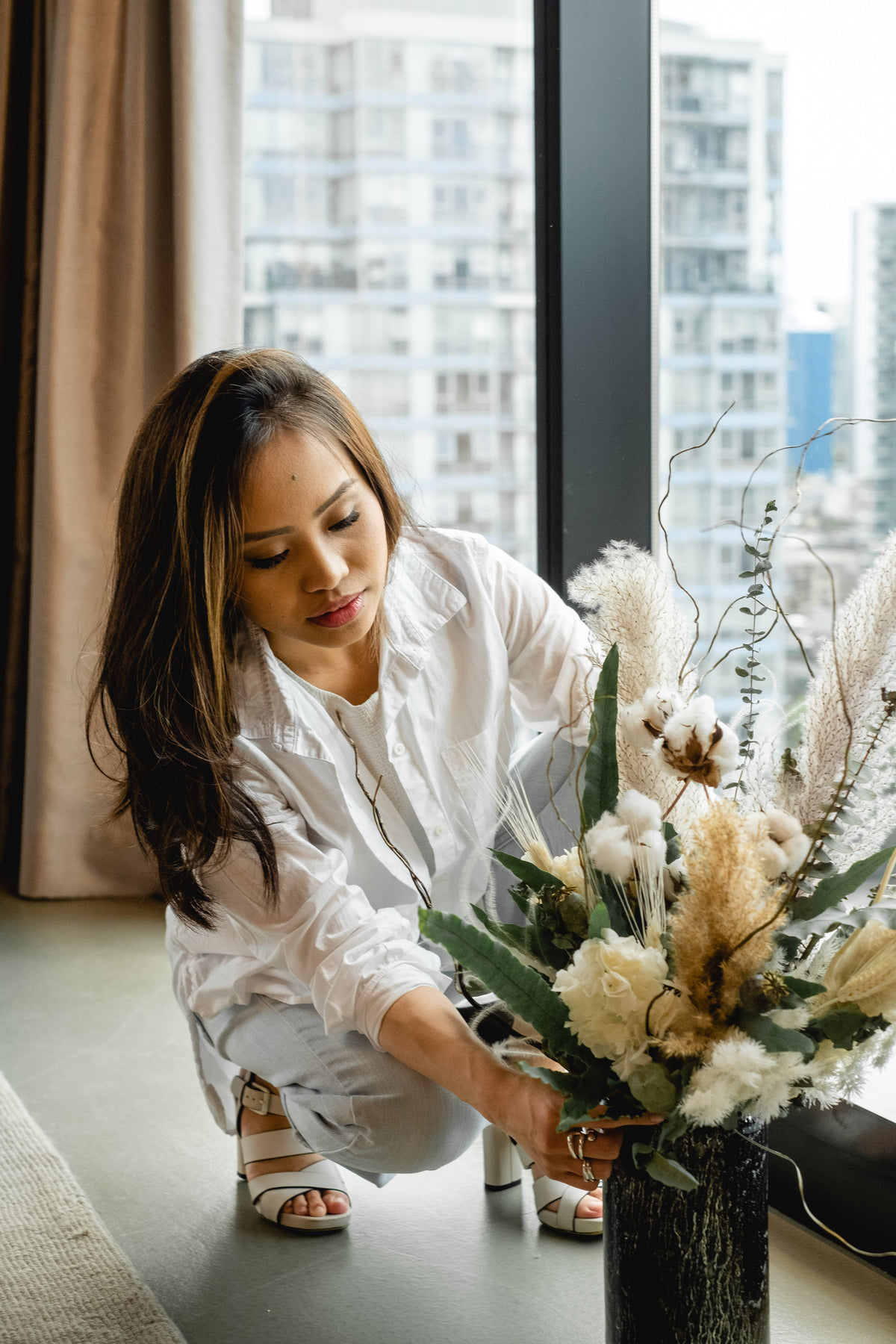 woman crouches to arrange flowers in a vase