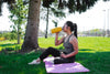 woman drinks from a yellow water bottle under a tree