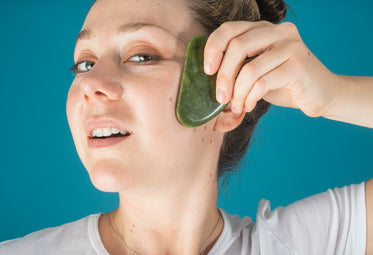 woman holds a jade face massager to her face