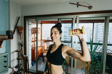 woman holds a weight up with one hand and smiles