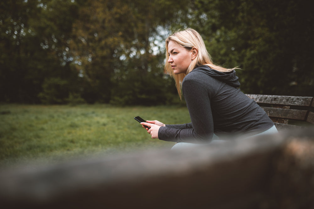 woman holds her cellphone and sits on a park bench