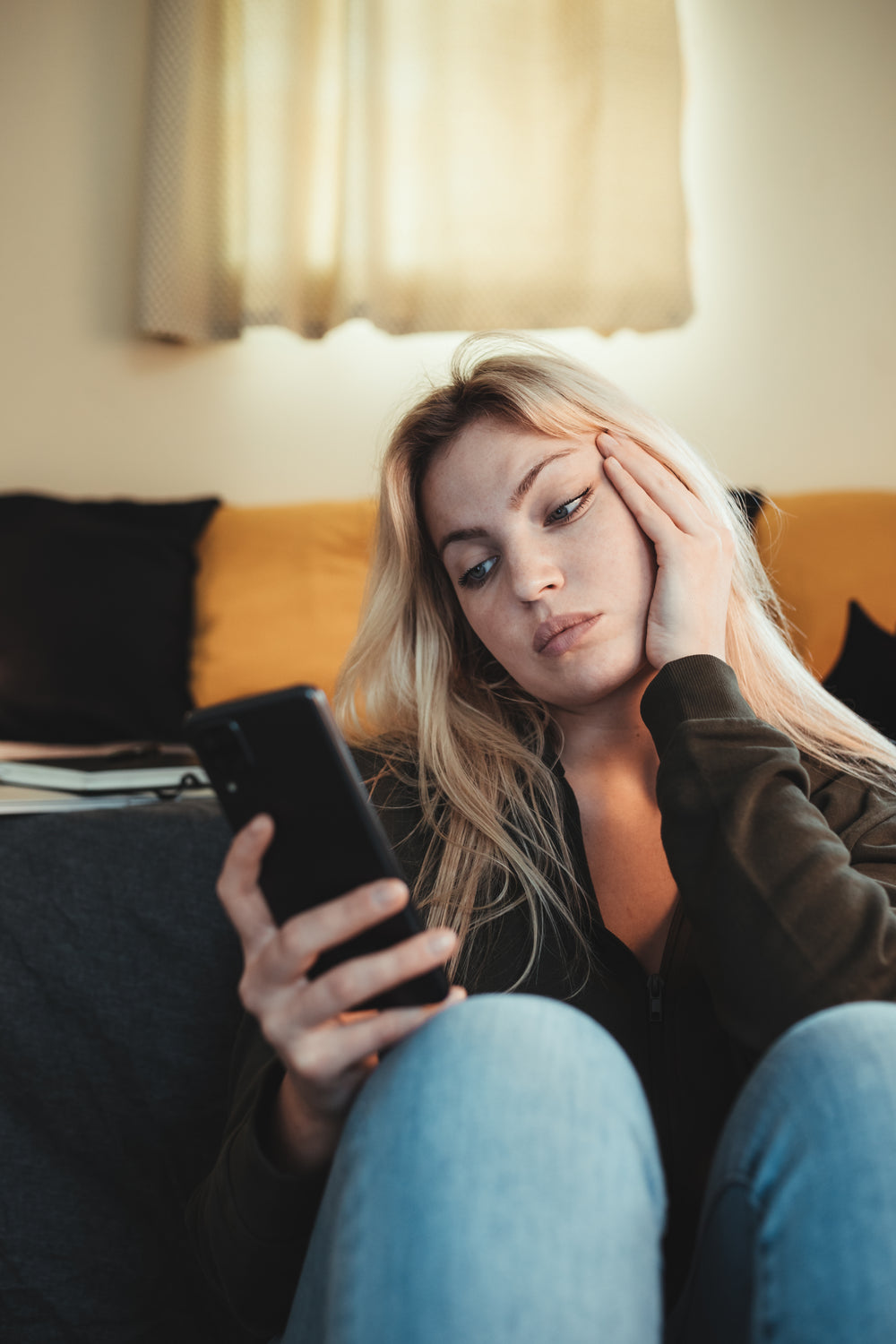 woman holds her hand to her cheek while she looks at phone