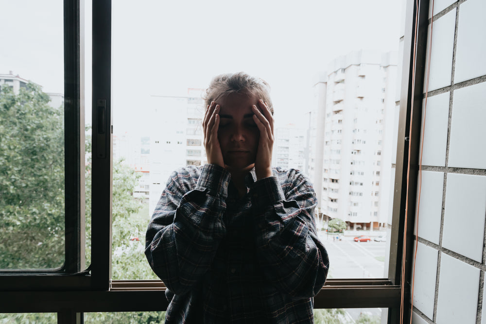 woman holds her hands to her facein front of a window