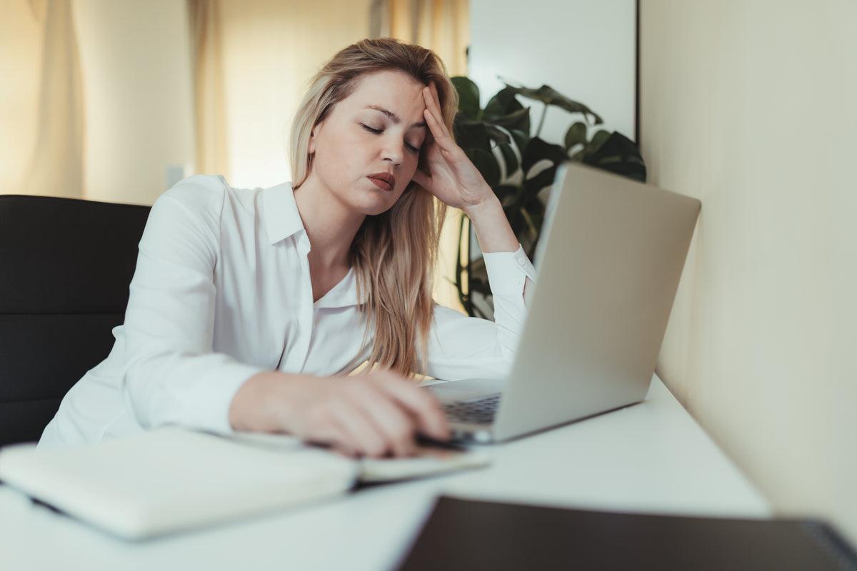 woman holds her head and closes her eyes while at work