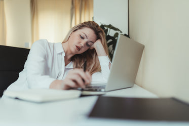 woman holds her head up with one hand and sits at her desk