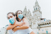 woman hugs man from behind while wearing blue facemask