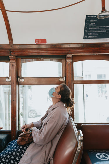 woman in a blue face mask rests on a brown bench