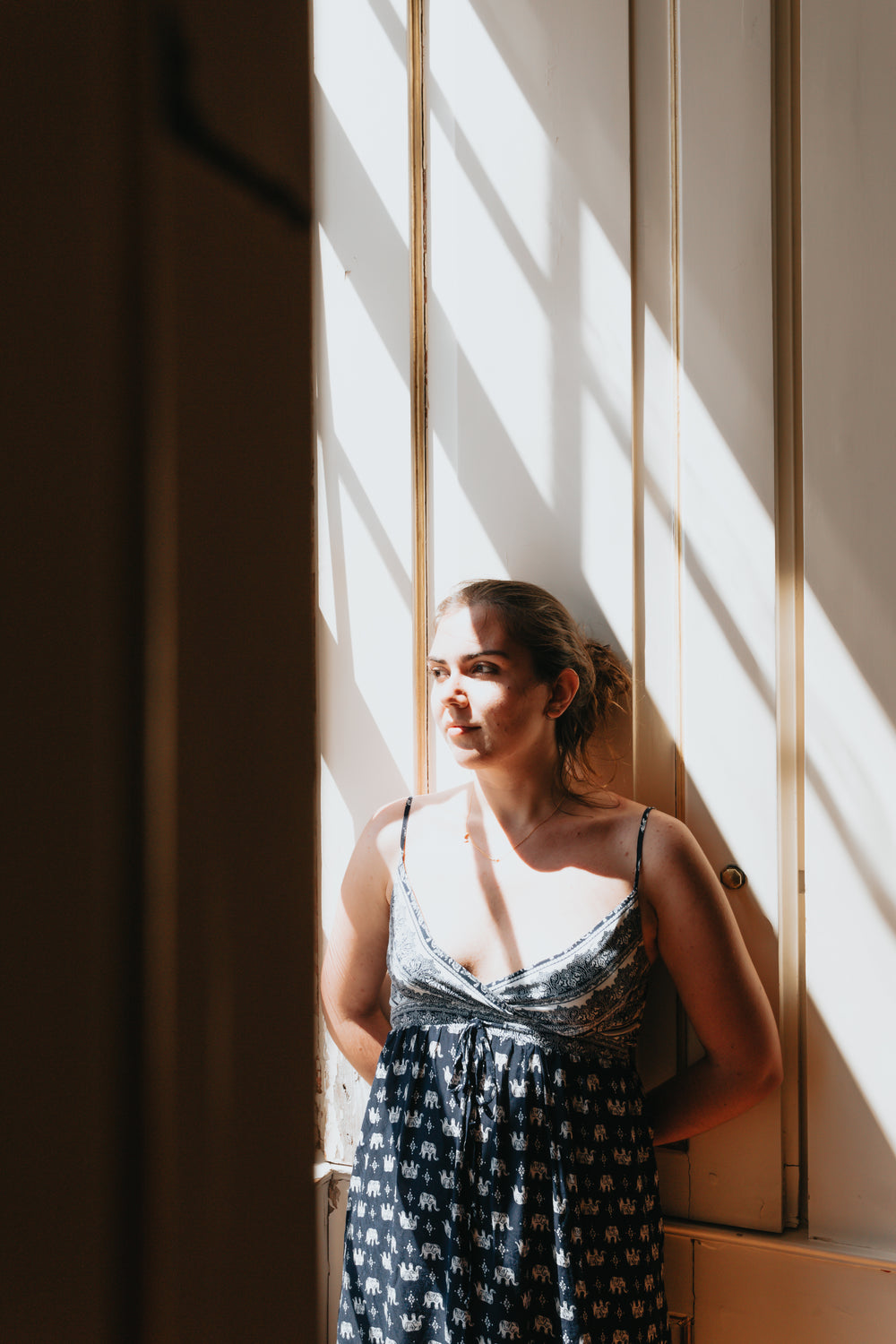 woman in a blue sundress leans against a white wall