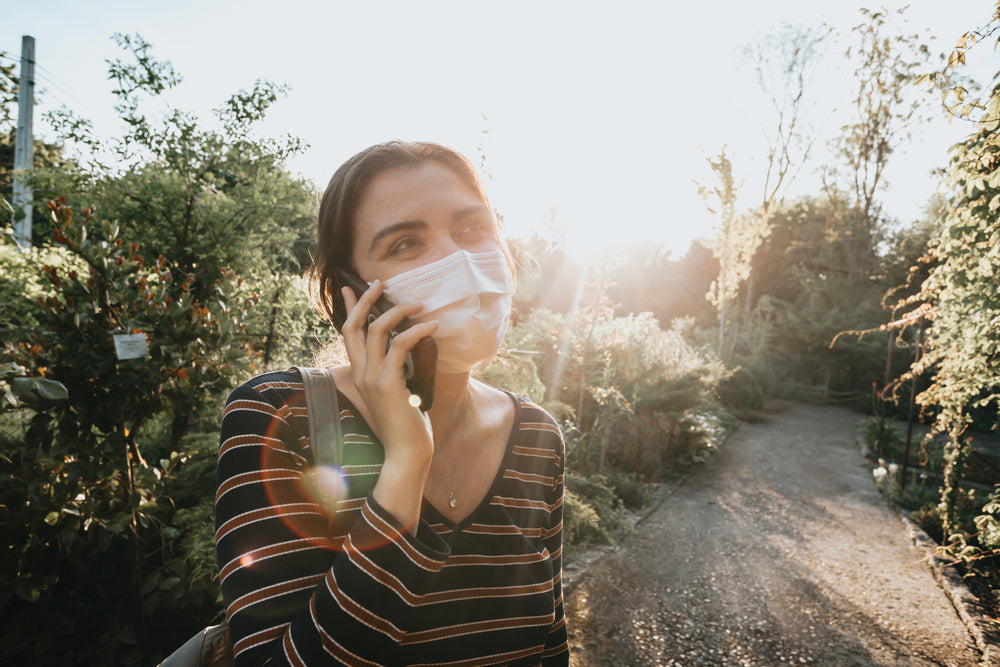 woman in a facemask talks on the phone outdoors