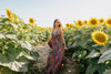 woman in a floral dress stands in a sunflower field