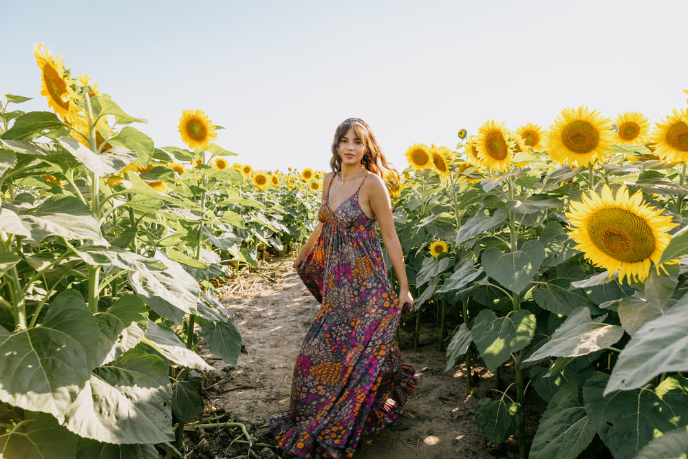 woman in a floral dress stands in a sunflower field