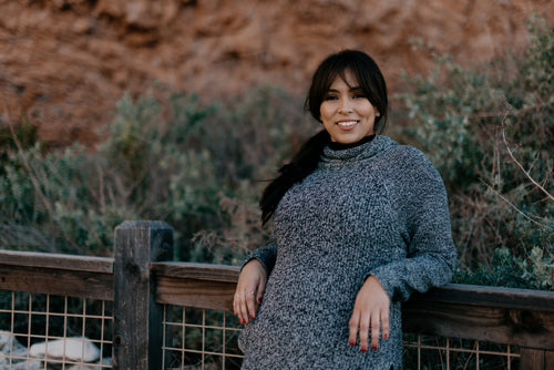 woman in a sweater smiles as she leans against a fence