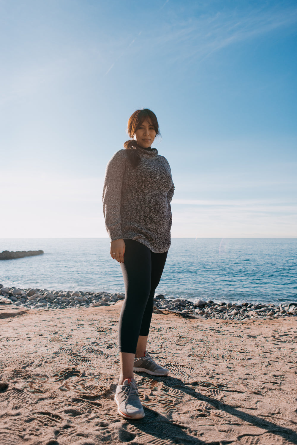 woman in a sweater stands on a beach in the morning