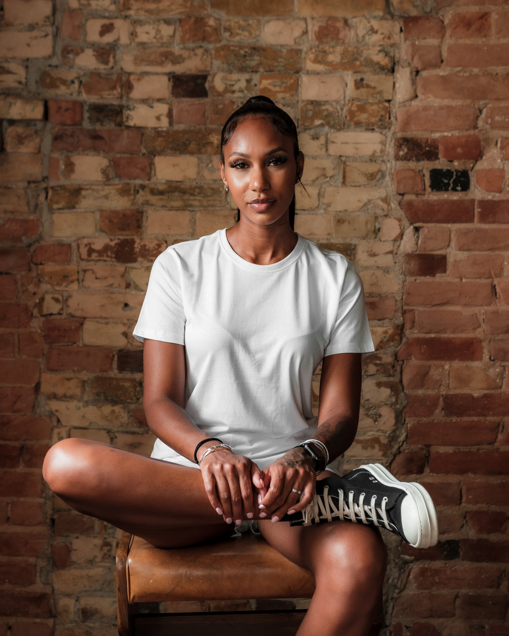 woman in a white shirt in front of a brick wall