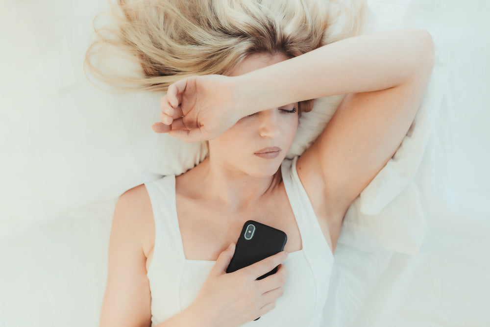 woman in bed on her cellphone with one arm up