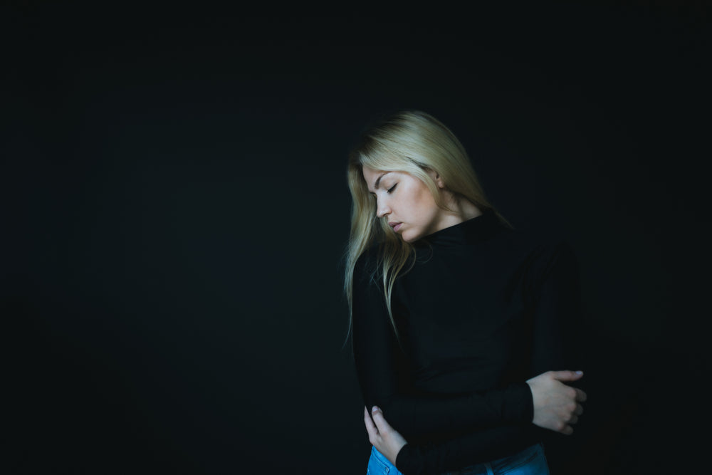 woman in black sweater hugs herself against black