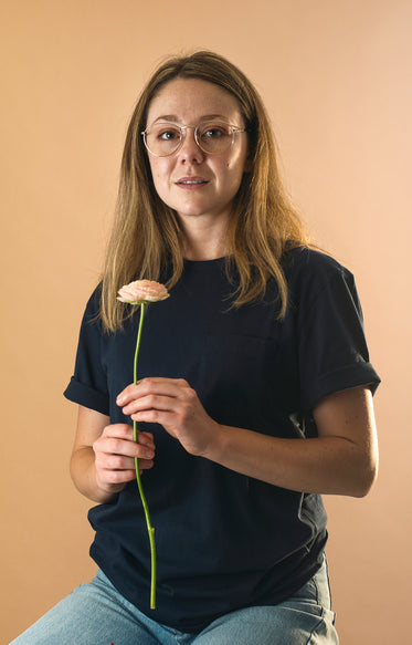 woman in blue holds a flower and looks at the camera