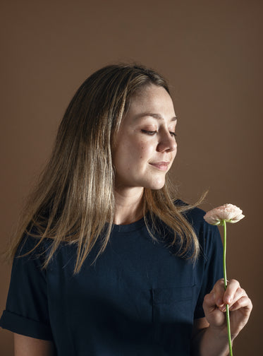 woman in blue with long brown hair holds a flower