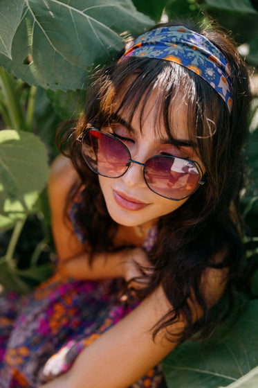 woman in bold sunglasses surrounded by green leaves