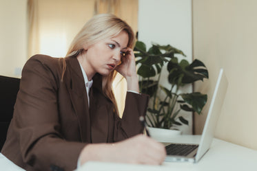 woman in brown suit sits and looks at her laptop screen