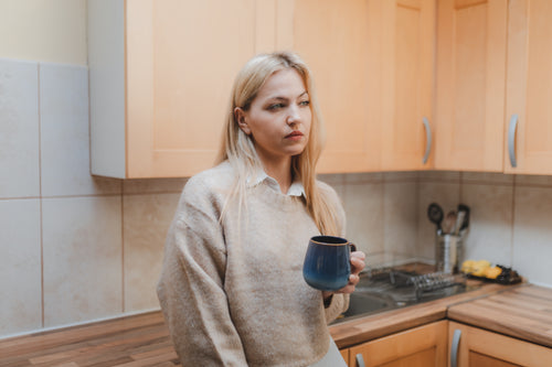 woman in collared shirt in the kitchen holding a mug