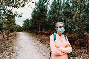 woman in face mask stands on a hiking trail